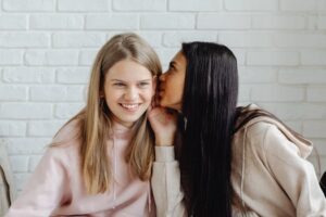 Two teenage girls whispering indoors, sharing secrets and friendship.