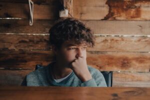 A young man sitting pensively against a rustic wooden backdrop, conveying introspection.