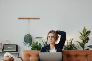 A woman sitting with a laptop on a comfortable sofa surrounded by indoor plants.